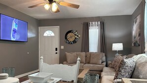 A living room with a television, a ceiling fan, a sofa, a coffee table, and a dining table with salt and pepper shakers. - corporate comfort suits  (Pocahontas)