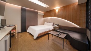 Ein modernes Hotelzimmer mit Bett, Schreibtisch, Stuhl, Sofa und Flachbildfernseher.