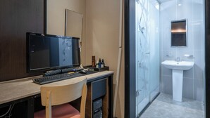 Ein modernes Badezimmer mit Dusche, Waschbecken und Spiegel. Ein Schreibtisch mit Computer und Stuhl ist ebenfalls vorhanden.