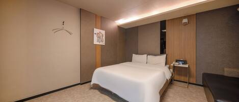 Una habitación de hotel con una cama grande, una mesita de noche con lámpara y un escritorio pequeño con computadora.