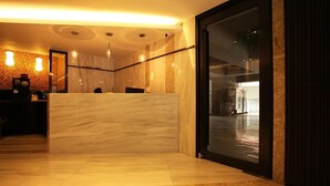 Ein Hotel-Empfangsbereich mit einem Marmor-Empfangstresen, einer großen Glastür, die zu einer geräumigen Lobby führt, und einem modernen Interieur.