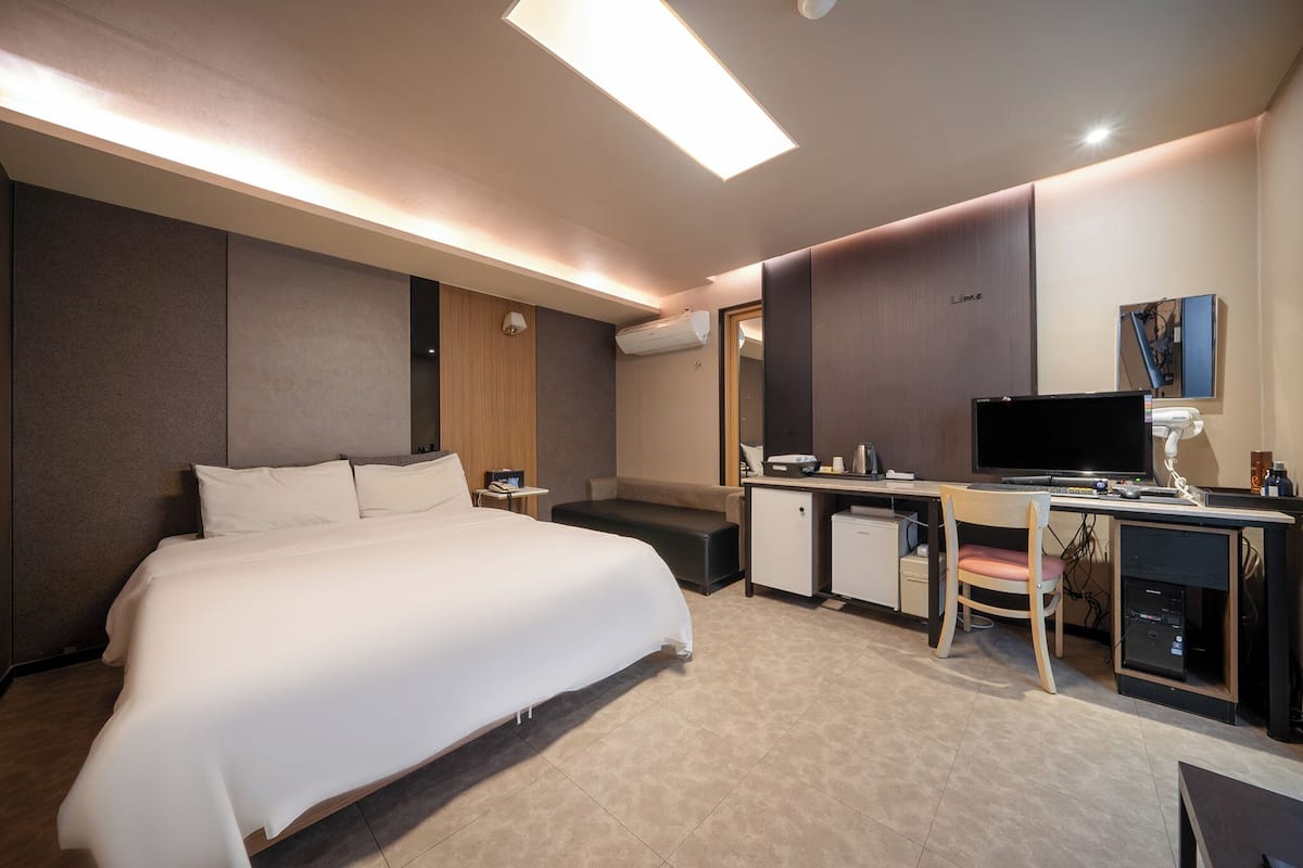 Une chambre d’hôtel moderne avec un grand lit, un bureau équipé d’un ordinateur, une chaise et un petit meuble de rangement.