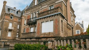 Un edificio histórico de varios pisos, con una combinación de ladrillo y piedra, ventanas amplias y un balcón destacado.