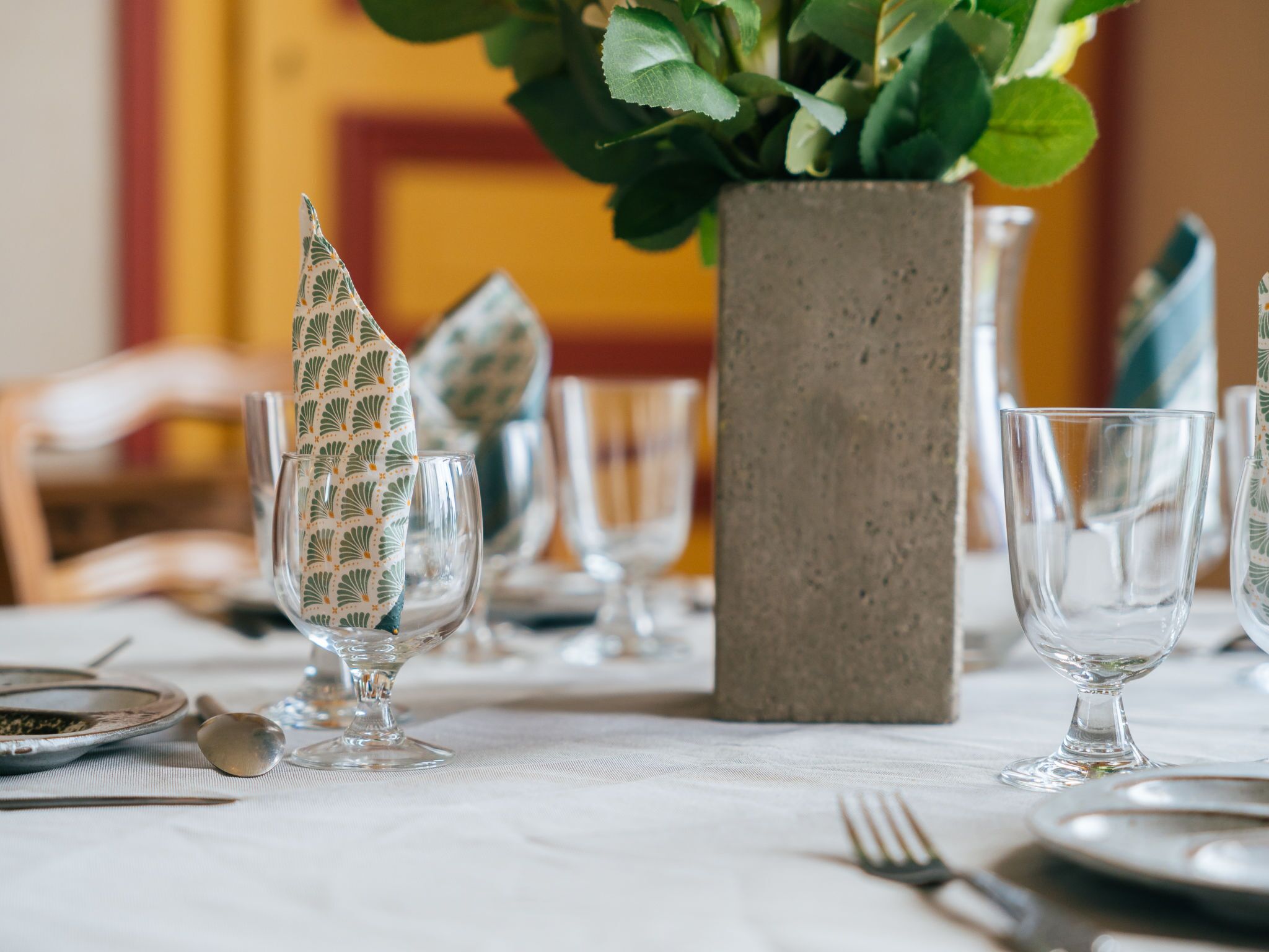 A table set with clear glassware, a patterned napkin holder, and a potted plant.