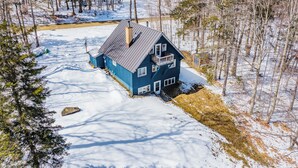 Ein blaues Haus mit Balkon, umgeben von Schnee und Bäumen.