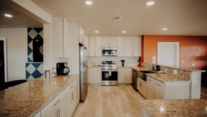 A modern kitchen with white cabinets, granite countertops, stainless steel appliances, and a microwave. - Casa Abuelo Loco, Terlingua's Premier Vacation Rental (Terlingua)