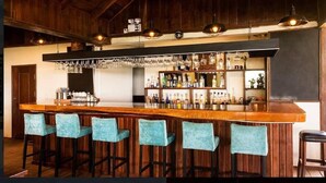 Zona de bar con mostrador de madera, varios taburetes y una gran variedad de botellas y copas.