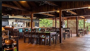 Un interior rústico de madera con una zona de bar, varios conjuntos de asientos y vistas al exterior.