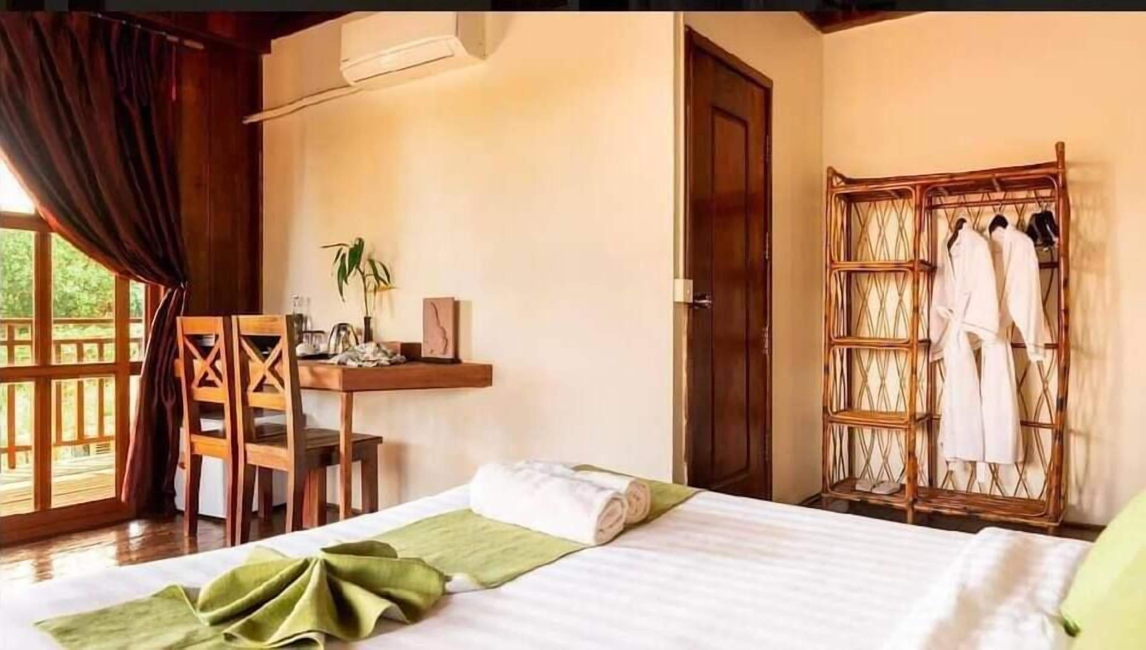 Ein Schlafzimmer mit Bett, Schreibtisch, Stuhl, Kleiderschrank und einem Fenster mit Vorhängen.