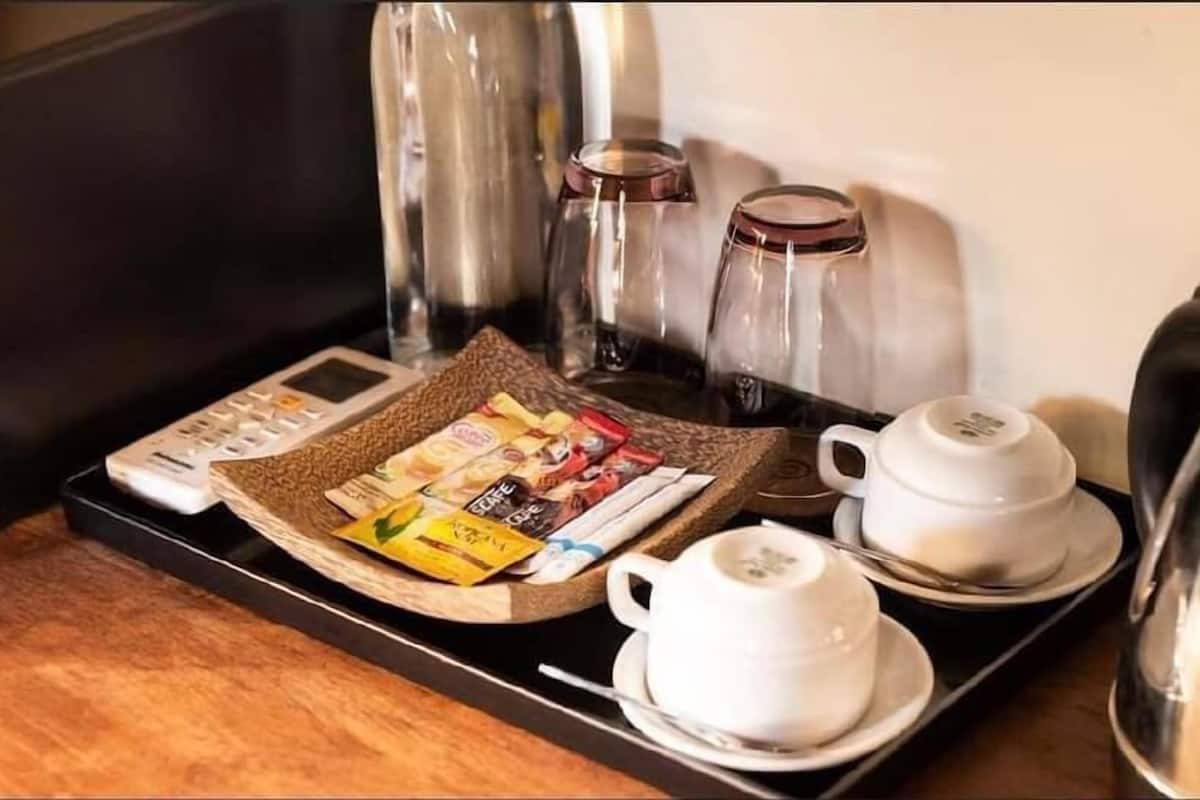 A tray with a coffee maker, two cups, a kettle, and a basket of coffee packets.