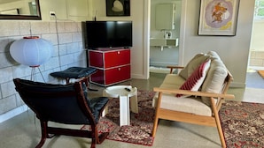 A living room with a TV, a red cabinet, a sofa, and a chair. - A private studio on Hobson Bay in historic Parnell. Central Auckland. (Auckland)