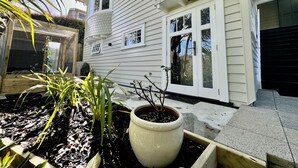 A house with a white exterior, a front porch with a potted plant, and a small garden area with mulch and plants. - A private studio on Hobson Bay in historic Parnell. Central Auckland. (Auckland)