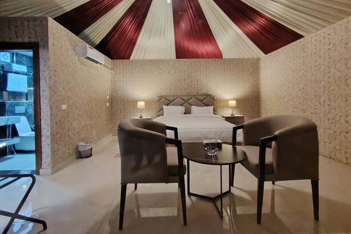 A hotel room with a bed, two chairs, a small table, and a ceiling with a unique design.