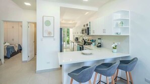 A modern kitchen with white cabinets, a central island with bar stools, and a view into the adjacent bedroom. - Family-Friendly 3BR | Pool | Near Tamarindo (Villareal)