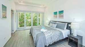 A modern bedroom with a large bed, a nightstand, and a view of greenery through the glass door. - Family-Friendly 3BR | Pool | Near Tamarindo (Villareal)