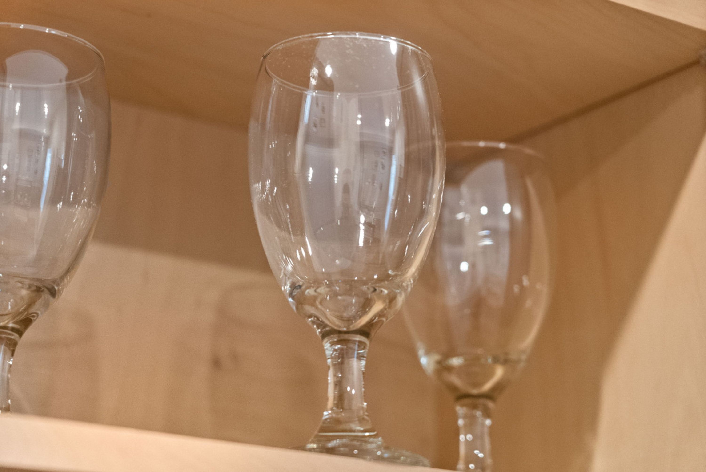 A close-up of three wine glasses on a shelf.