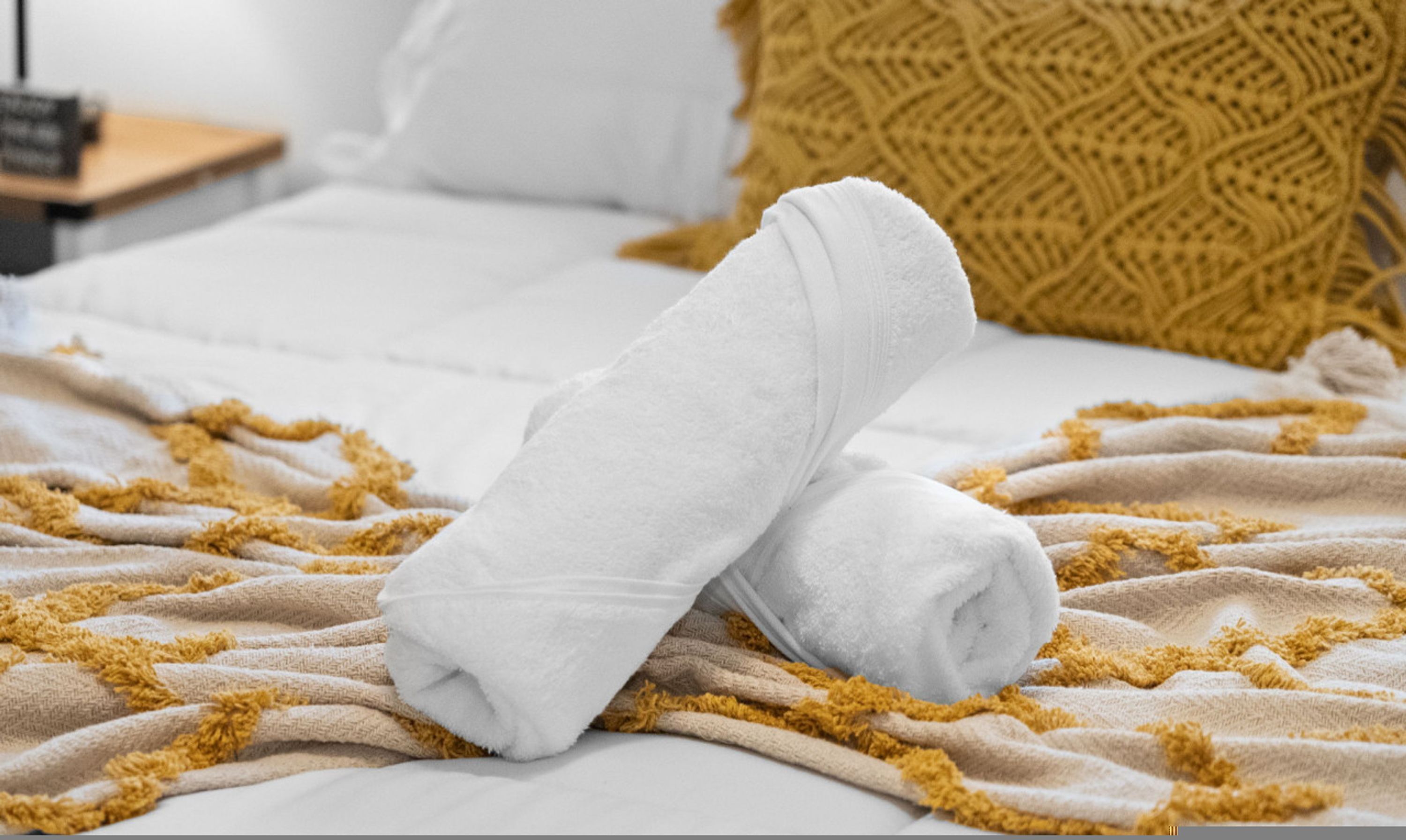 Una cama bien tendida con una toalla blanca, un edredón color beige y una almohada amarilla estampada.