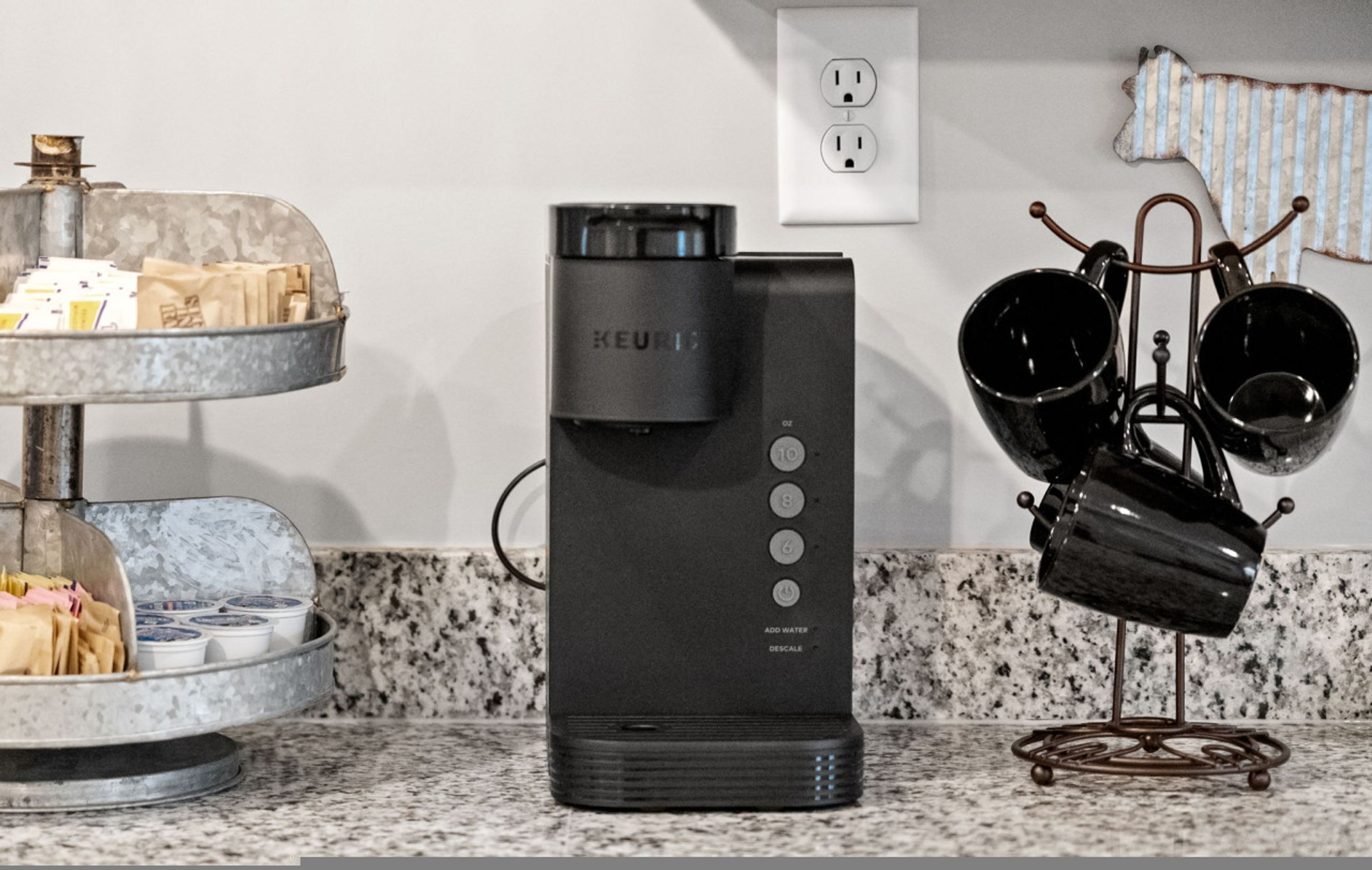 Una cocina con cafetera, hervidor y jarra de café sobre un soporte.