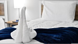 A neatly made bed with white linens and a dark blue blanket.
