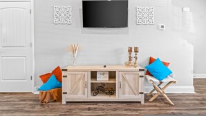 A modern living room with a wooden cabinet, a mounted TV, decorative wall art, and a folding chair.