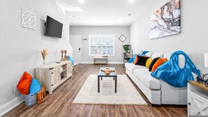 A modern living room with a flat-screen TV, a coffee table, and a sofa with colorful cushions.