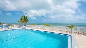 Une piscine à l’eau d’un bleu cristallin, entourée d’une clôture blanche et de palmiers.