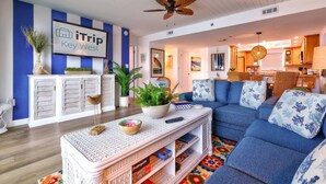 Un salon avec un canapé bleu, des meubles blancs et un ventilateur de plafond.