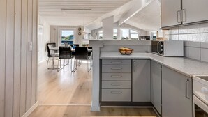 A modern kitchen with grey cabinets, a microwave, and a dining area with a table and chairs. - "Jaana" - 10m from the sea by Interhome (Blåvand)