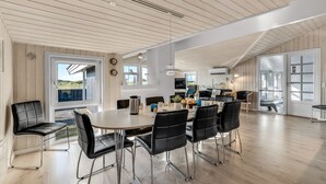 A spacious dining area with a large table and modern chairs, a kitchen in the background, and large windows offering views. - "Jaana" - 10m from the sea by Interhome (Blåvand)
