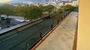 En balkon med gelænder af glas, der giver udsigt over et bybillede med bygninger og et fjerntliggende bjerg.