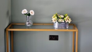 Una habitación con pared verde, una consola de madera, una lámpara de pared y un enchufe.