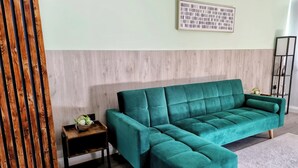 Un sofá seccional color turquesa con patas de madera, una pequeña mesita de madera con una cesta, y un cuadro abstracto enmarcado en la pared.
