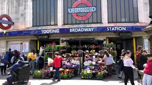Un mercado de flores frente a un edificio con un letrero que dice 'TOOTING BROADWAY STATION'.