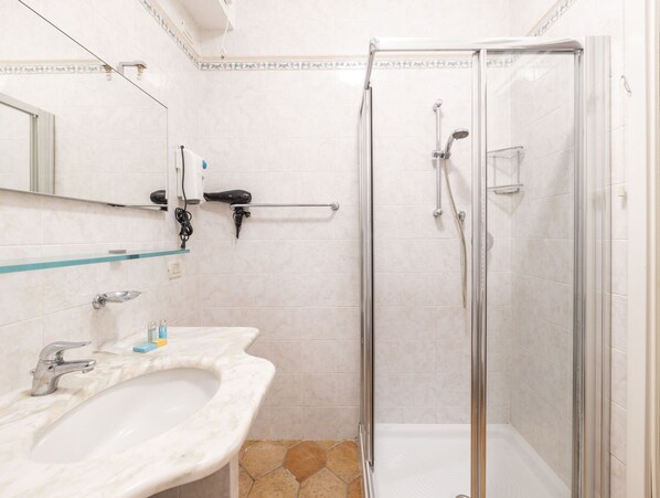 A bathroom with a glass-enclosed shower, a marble sink, and a mirror above the sink.
