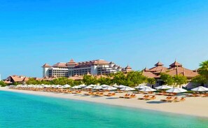 Relax on the beach with lounge chairs and umbrellas, surrounded by lush greenery and palm trees.