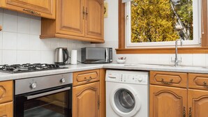 Una cocina con armarios de madera, microondas, estufa, lavavajillas y lavadora.