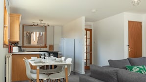 Un espacio habitable compacto con comedor, kitchenette y un sofá gris con un cojín verde.