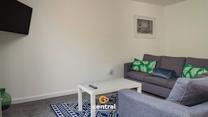 Una sala de estar con un sofá gris, una mesa de centro blanca, un cuadro en la pared y un tapete azul estampado.