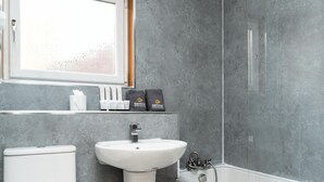 Un baño con un lavamanos blanco, un inodoro y una ducha. Hay dos bolsas etiquetadas "central" en el estante sobre el lavamanos.