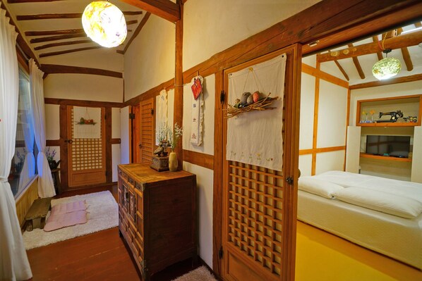 Ein traditioneller japanischer Raum mit Tatami-Böden, einem Holztisch mit Vase, einem Bett mit Futon und einer Schiebetür mit dekorativer Aufhängung.