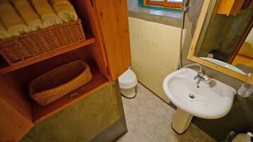 A bathroom with a white sink, a toilet, a wicker basket shelf, and a window with a view of the outside.