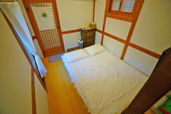 A small, traditional Japanese-style room with a tatami mat floor, a low wooden bed with white bedding, a small wooden cabinet, and a shoji screen door. - sky-kiwa (Jeonju)