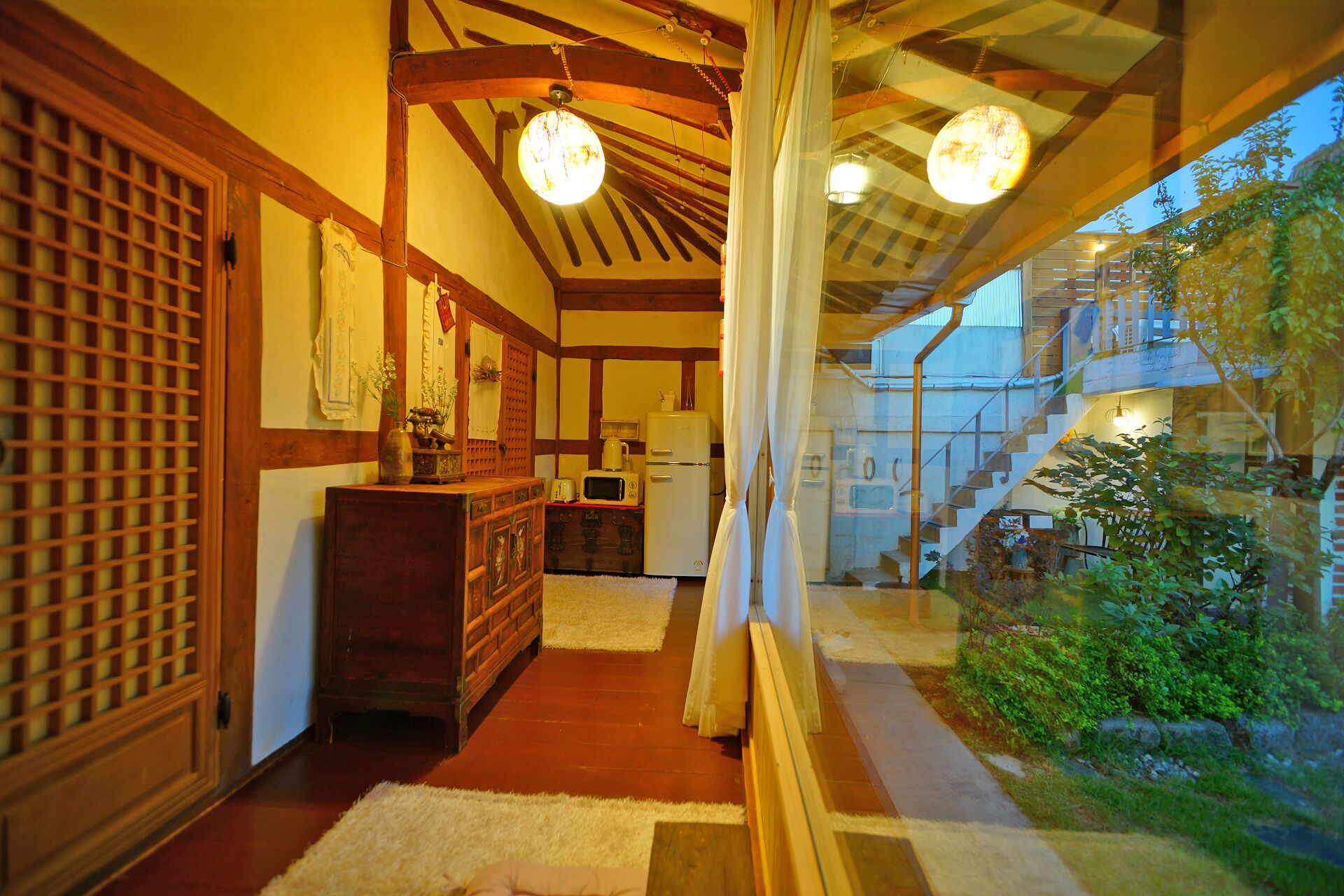 Un interior japonés tradicional con suelo de tatami, un armario de madera, un refrigerador y vistas a un jardín por una puerta de cristal.