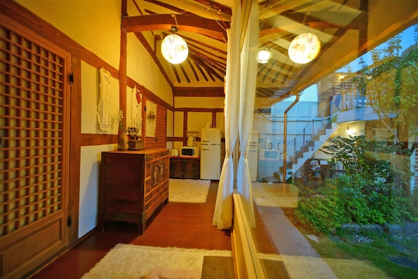 A traditional Japanese-style interior with tatami flooring, a wooden cabinet, a refrigerator, and a view of a garden through a glass door. - sky-kiwa (Jeonju)