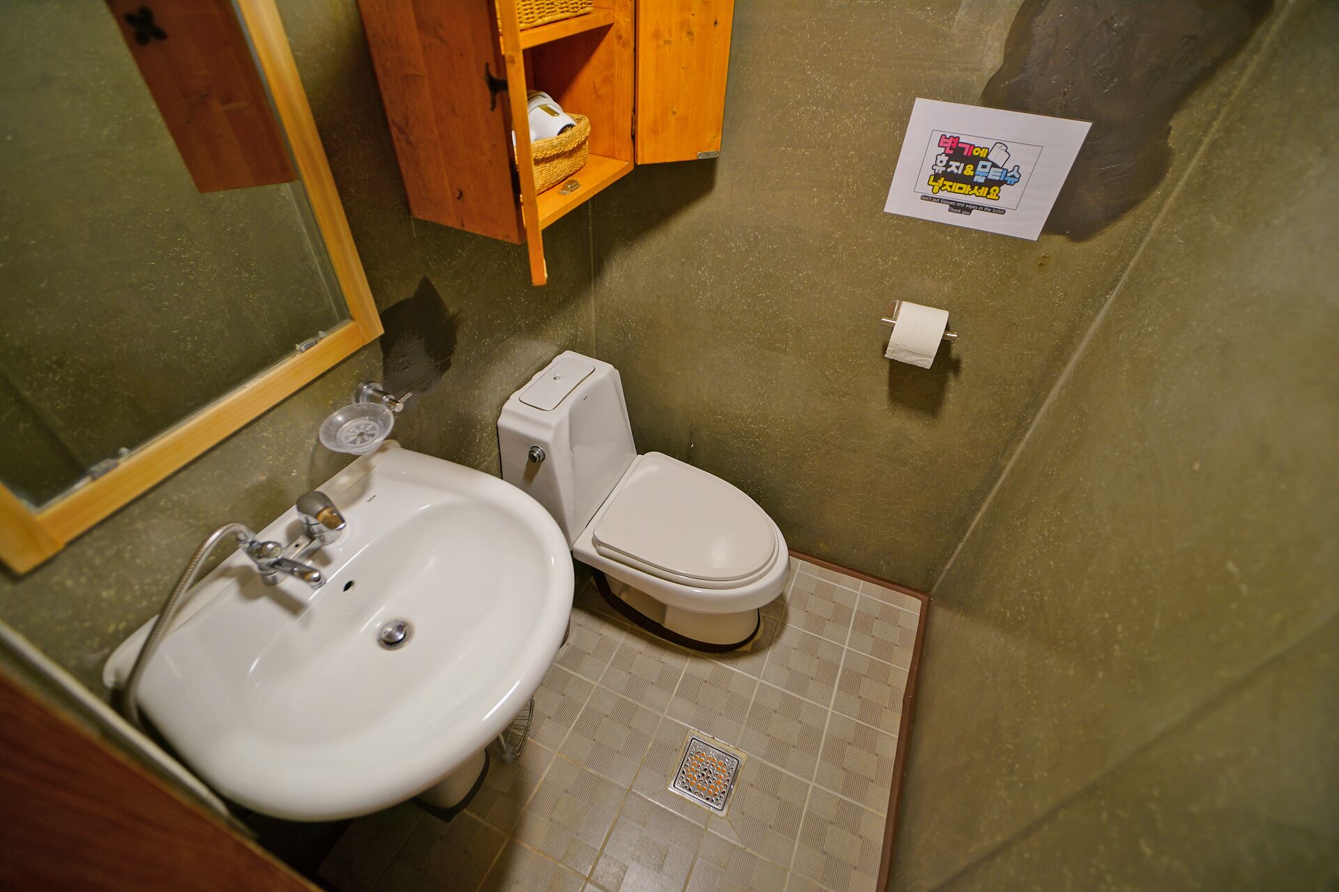 A small bathroom with a sink, toilet, and a wooden cabinet with a basket.