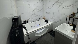 Ein modernes Badezimmer mit Marmorwand, freistehender Badewanne, Waschbecken und Toilette.