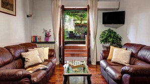 Un salon avec deux canapés en cuir, une table basse sur laquelle sont posés des pièces d’échecs, un téléviseur et un escalier menant à un espace extérieur agrémenté de plantes.
