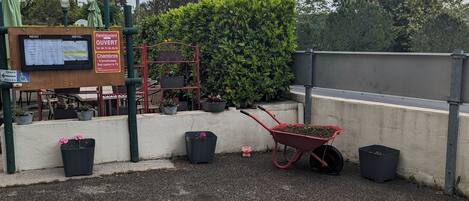 A gravel area with a wheelbarrow, potted plants, and a signboard with hotel and restaurant information.