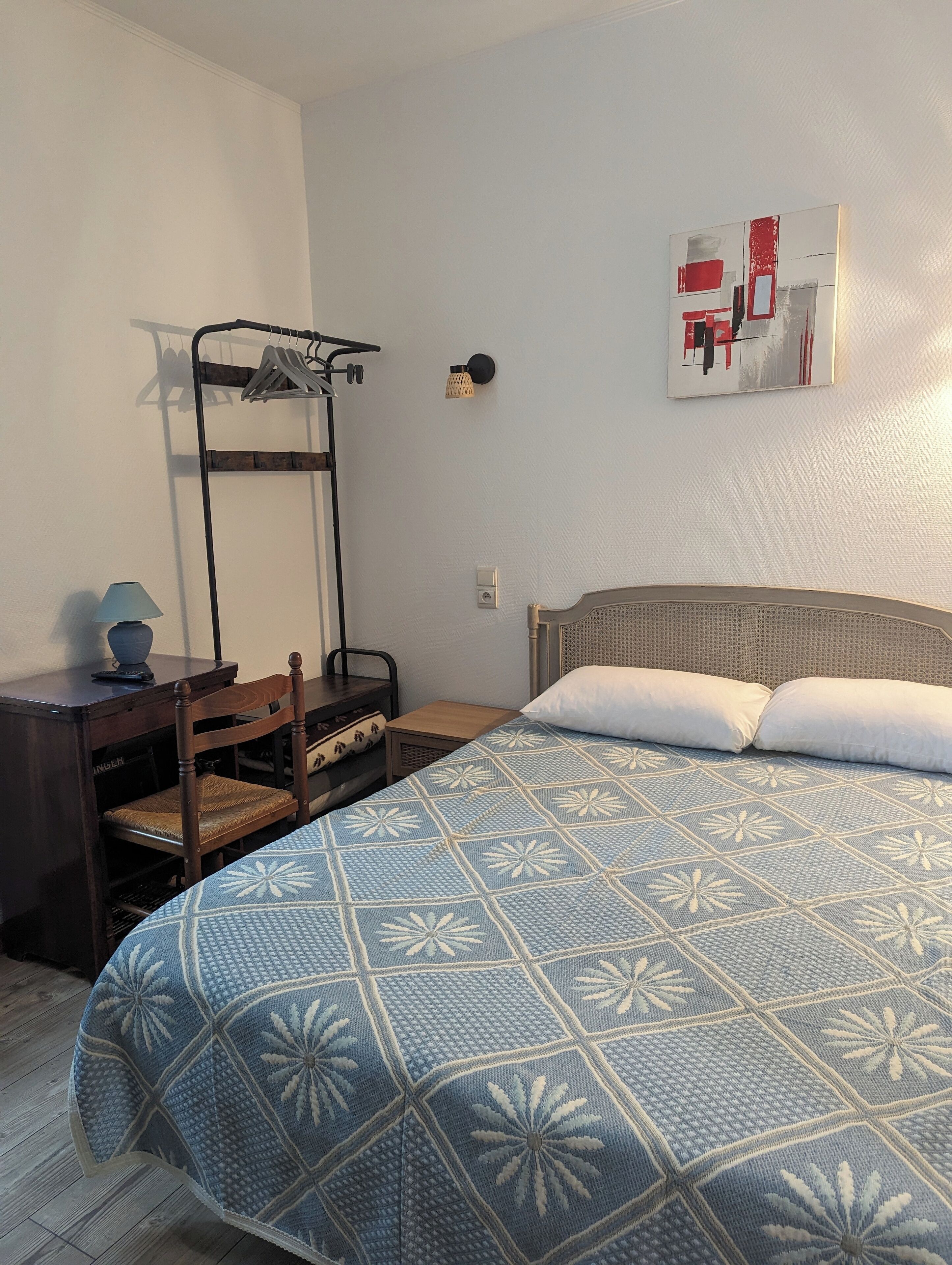 Une chambre avec un lit superposé, une table de chevet avec une lampe, une chaise et un lit recouvert d’une couvre-lit à motifs.