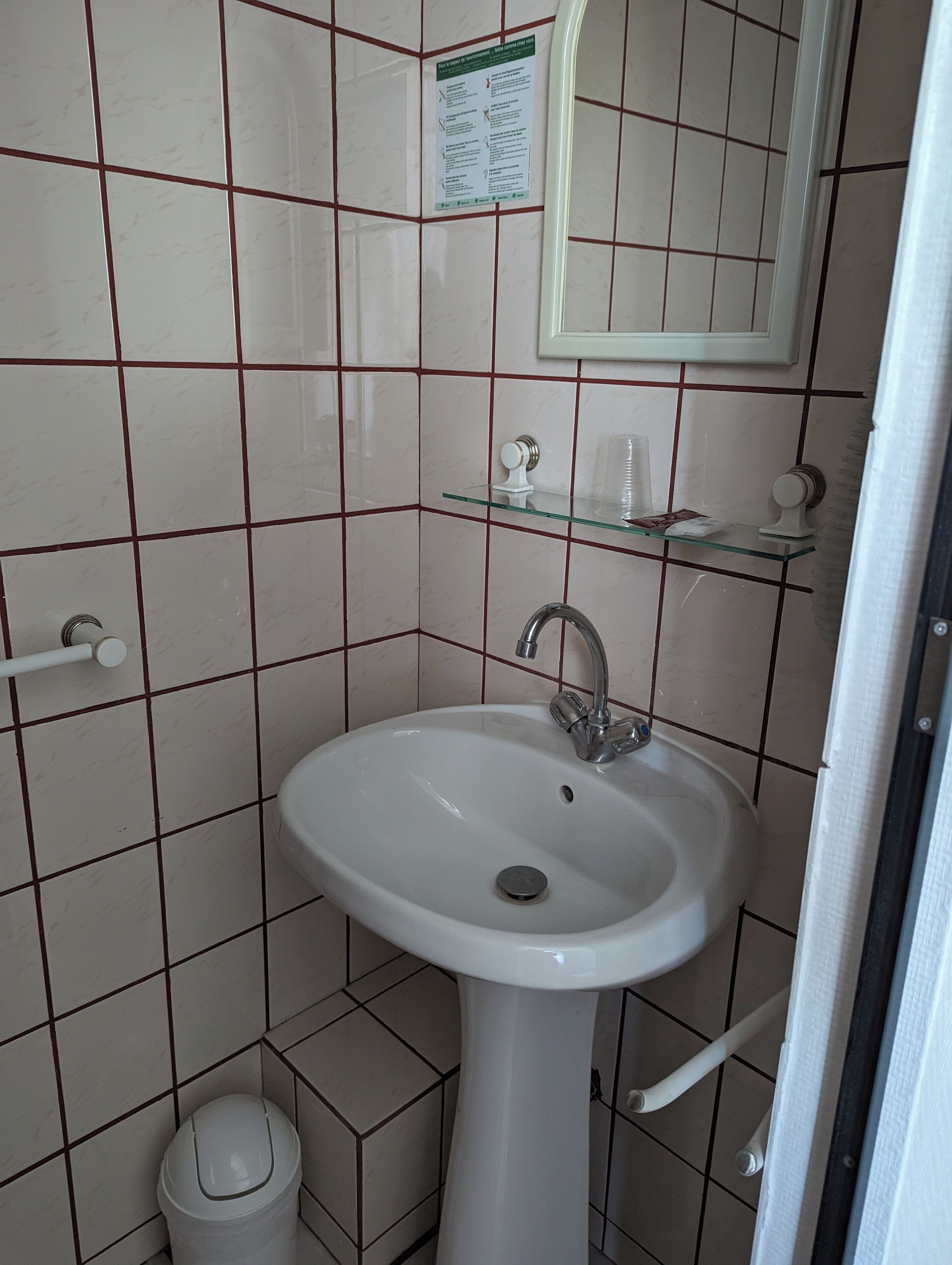 Een badkamer met een witte wastafel, een spiegel en een glazen plank.